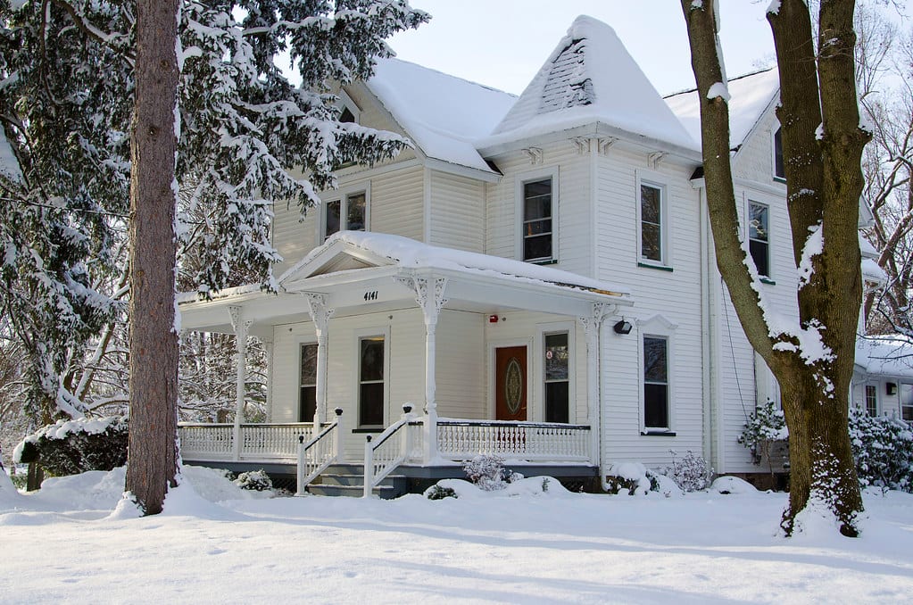 A snow covered Victorian home with white clapboard siding.