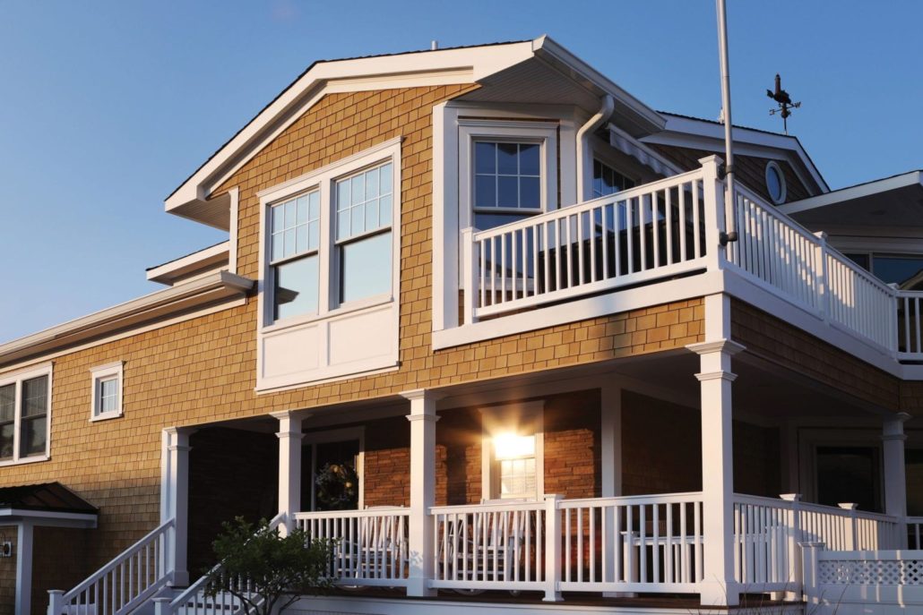 A home with tan Beach House shake siding and white trim and railings on the porch and balcony.