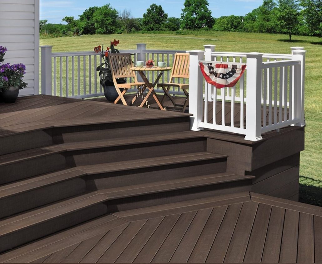 A brown composite deck and stairs with white railings and a small wooden table with 2 chairs.