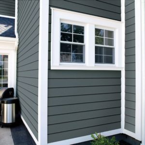 A wall with dark gray clapboard siding, white trim, and a white window.