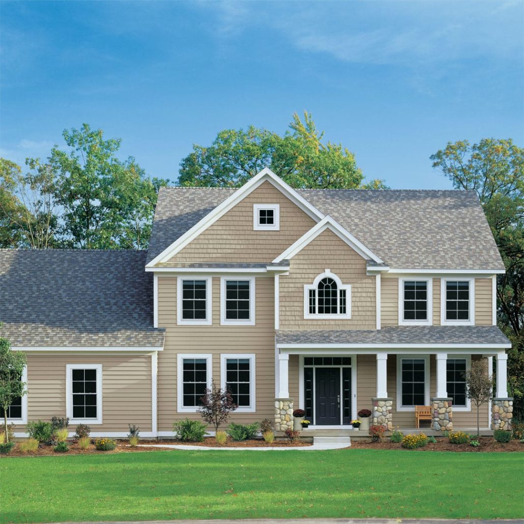 A large home with tan clapboard and shake siding and gray roofing shingles.
