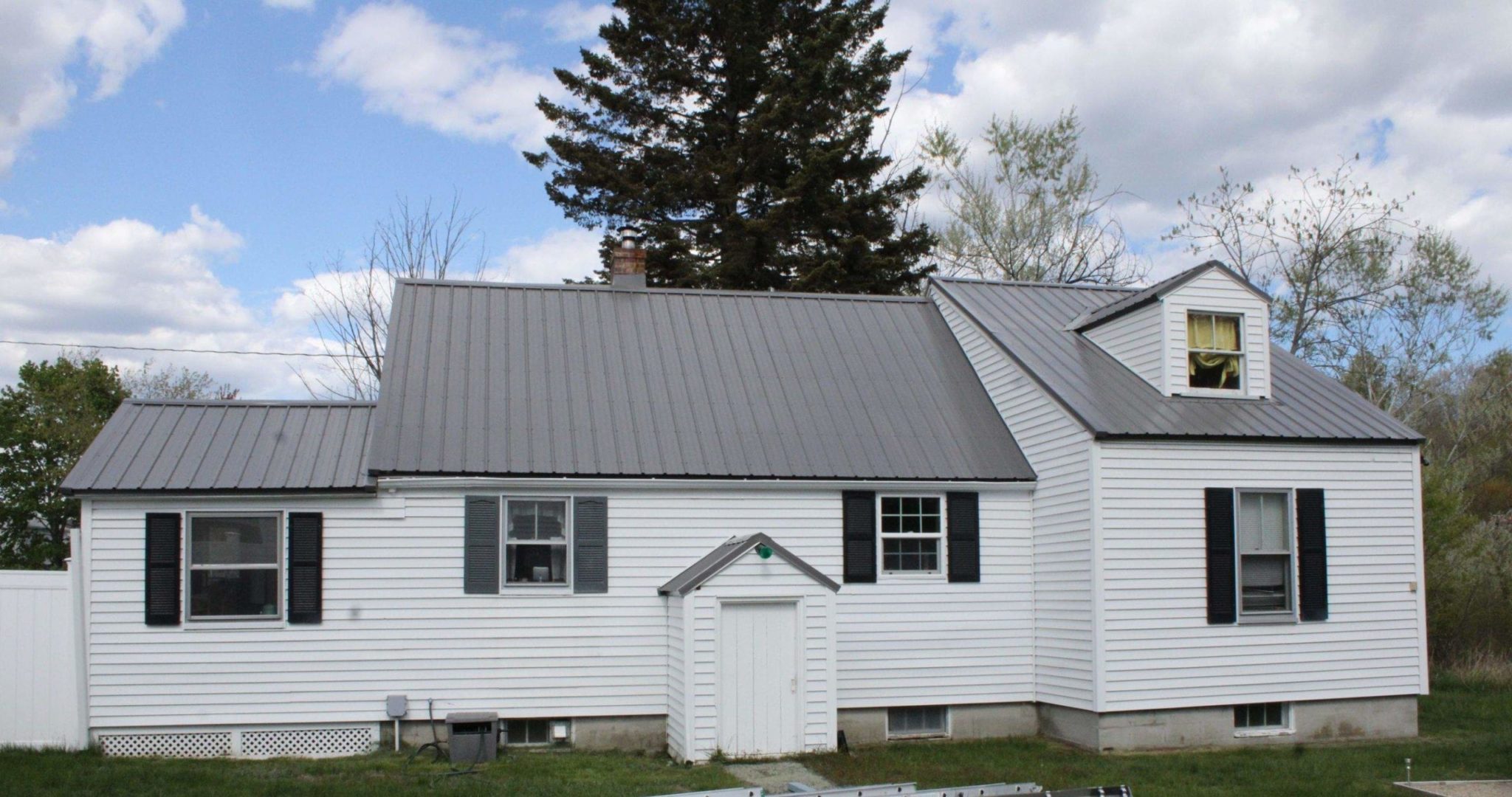 A white home with gray metal roofing and black shutters.