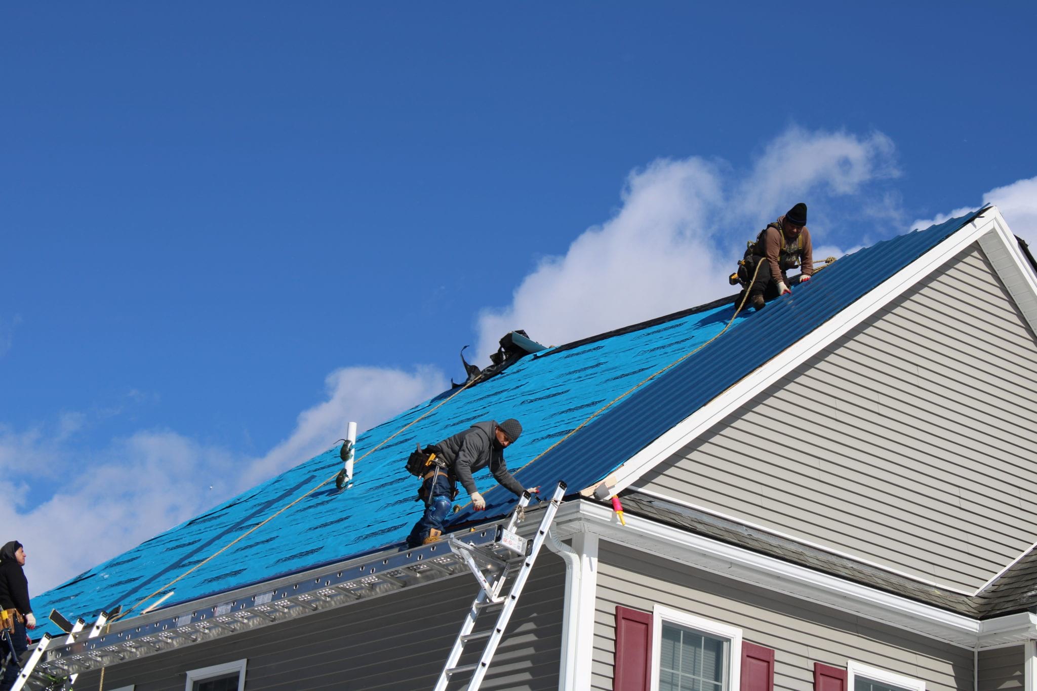 3 workers applying metal panels to a roof.