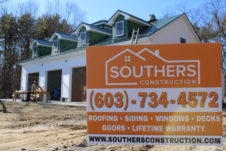 A Southers Construction sign placed in front of a home with workers installing a new green metal roof in Danville, NH.