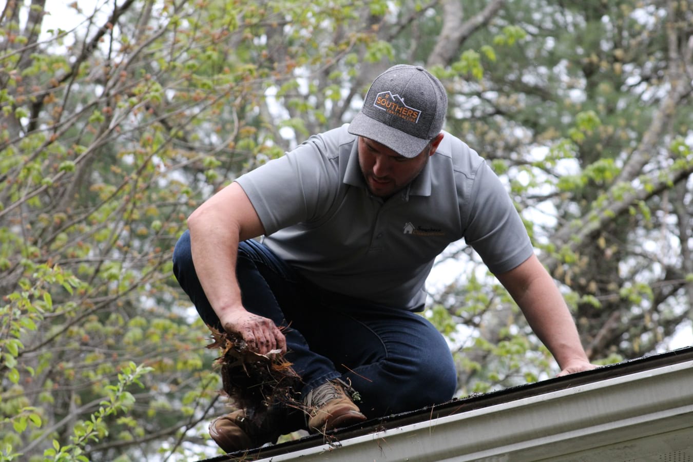 A man in a Southers Construction hat removing leaves from an asphalt shingle roof in Epping, NH.