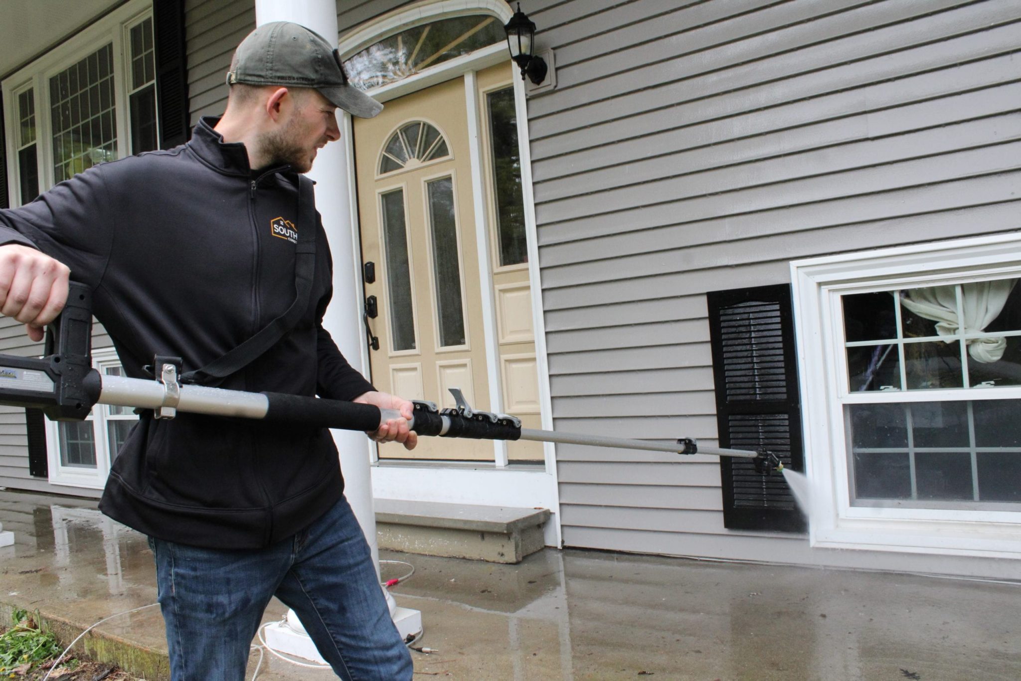 A man power washing a home's vinyl siding.