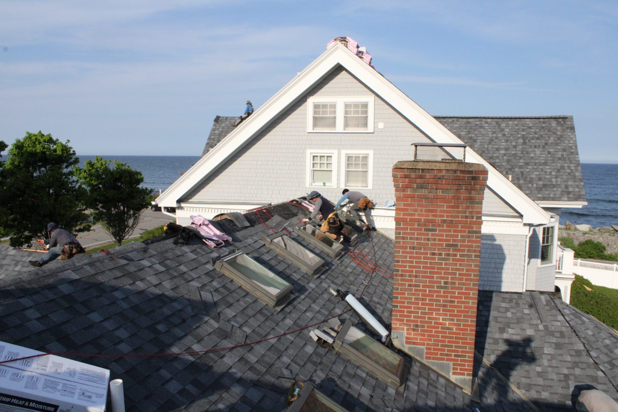 Roofers replacing a shingled roof on a home in Rye, NH.