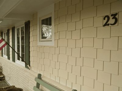 Beige HardieShingle shake siding on a home with white trim and green shutters.