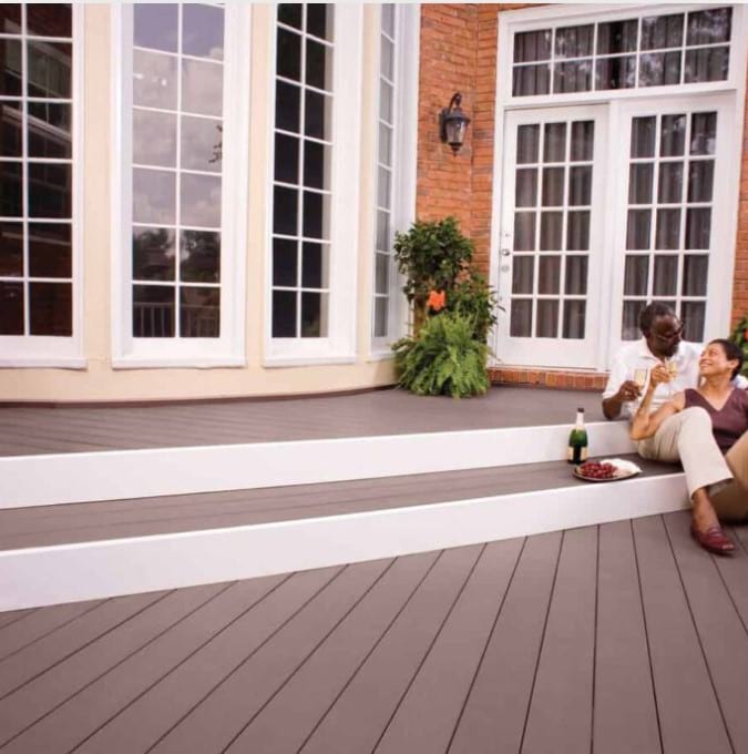 A couple sitting on a brown composite deck with white trim. They are drinking wine and smiling at each other.