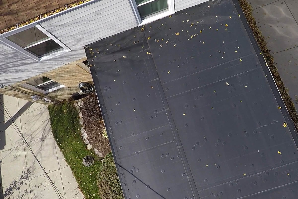 The top of a home's flat black rubber roof with leaves on it.
