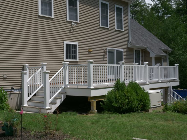 A pressure treated wood deck with white railings on the backside of a tan home in Strafford, NH.