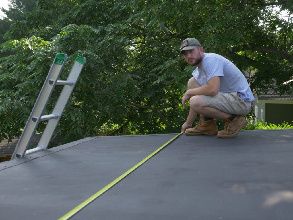 A man holding a tape measure on a flat black roof in Portsmouth, NH.