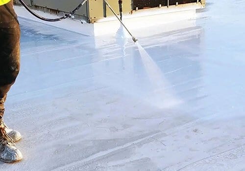 A person spraying silicone roof coating onto a flat roof.