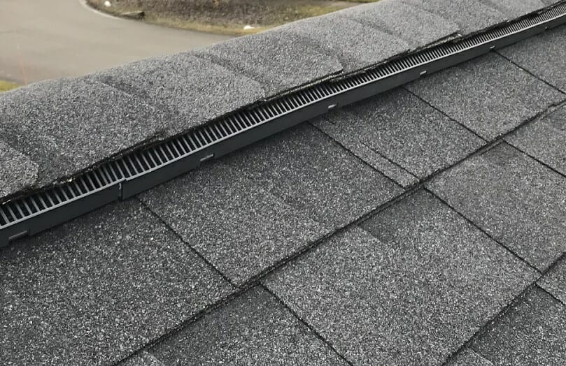 A ridge vent on the peak of a roof with gray shingles.