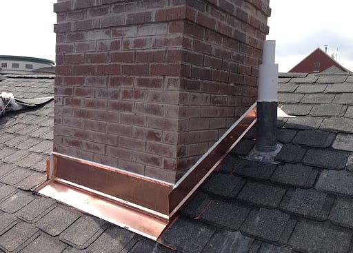A brick chimney on a roof with new copper flashing.