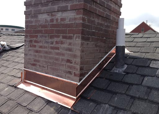 A brick chimney on a roof with new copper flashing.