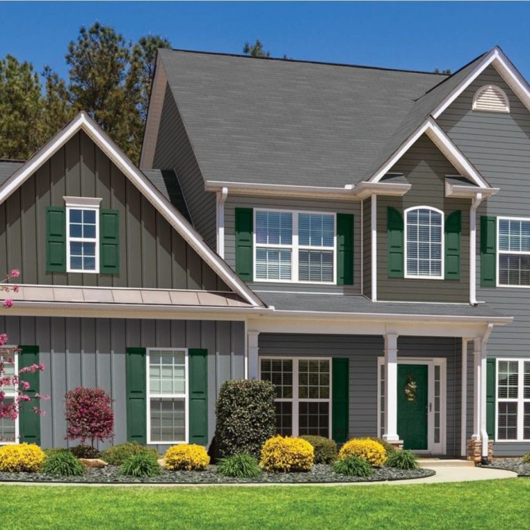 A large 2 story home with gray clapboard and board & batten siding. There are green shutters around the windows.