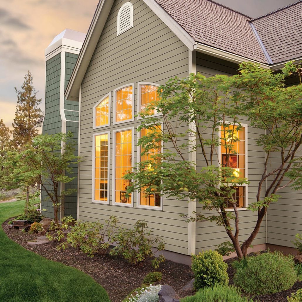 A home with tan siding and a garden planted outside a large window.
