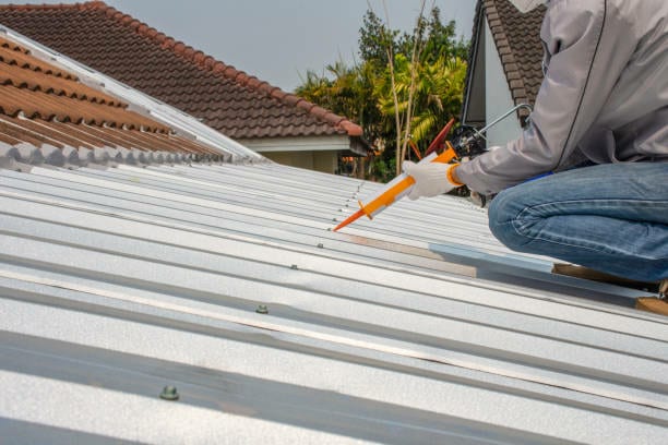 A person adding silicone caulking to a metal roof.