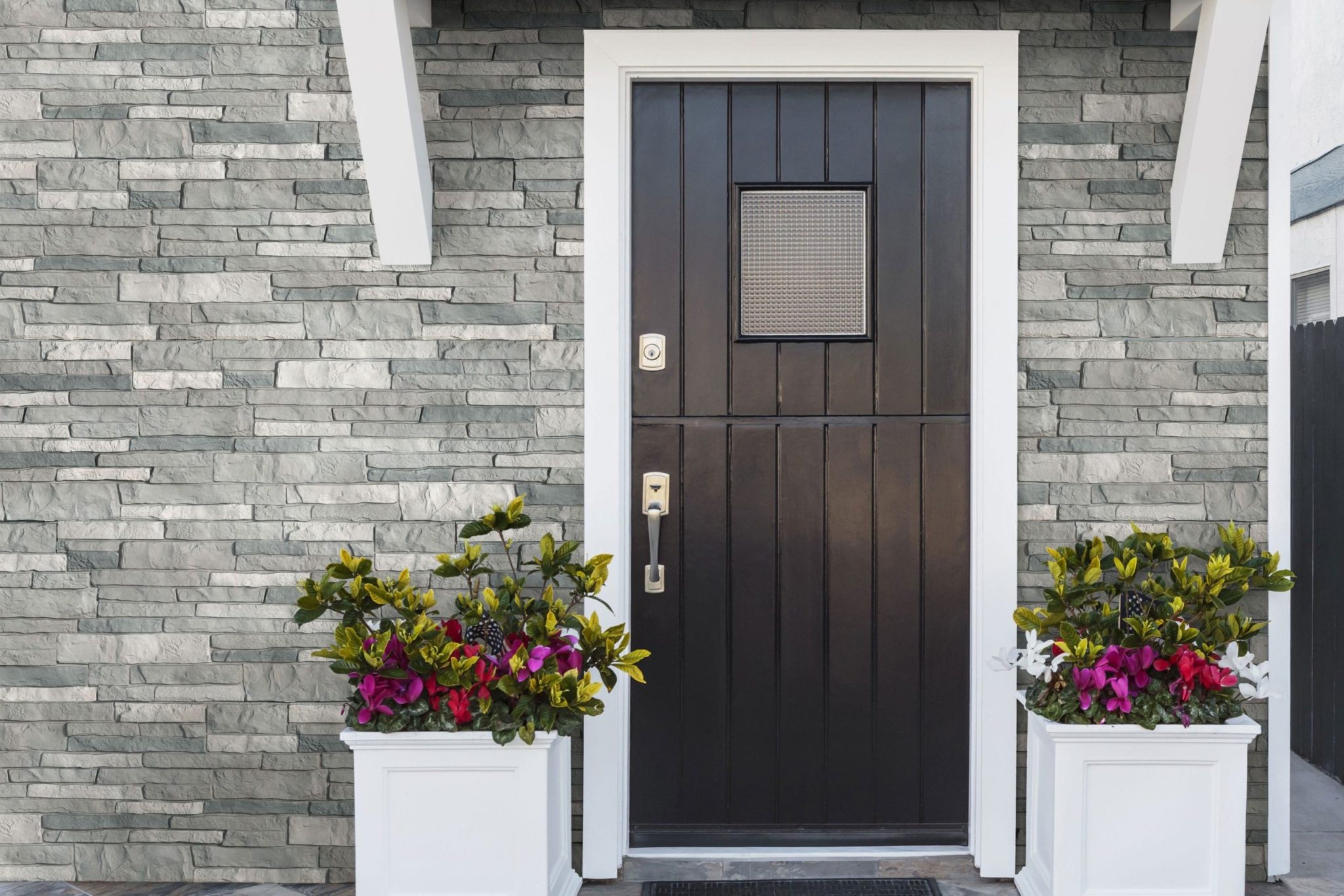 A dark brown wooden entry door surrounded by gray TandoStone siding.