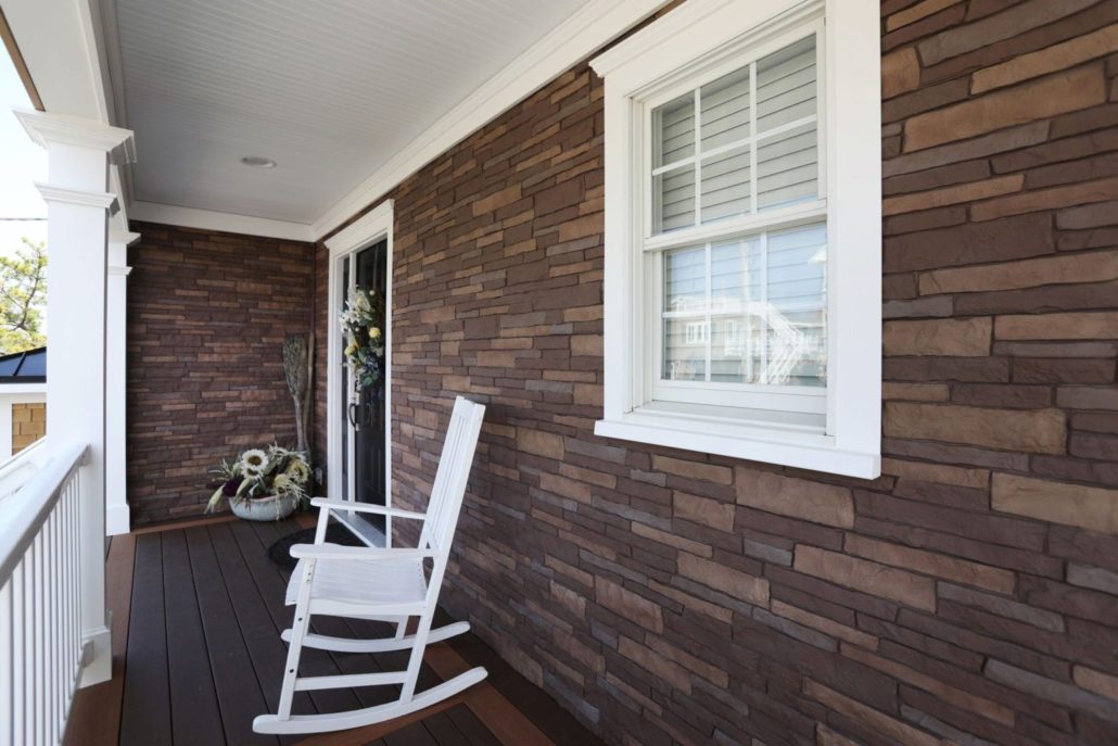 A home with brown TandoStone siding and white trim and railings. There is a white rocking chair on the porch.
