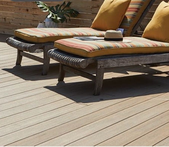 Warm brown composite decking with 2 lounge chairs. The chair on the right has a straw hat and a magazine on it.