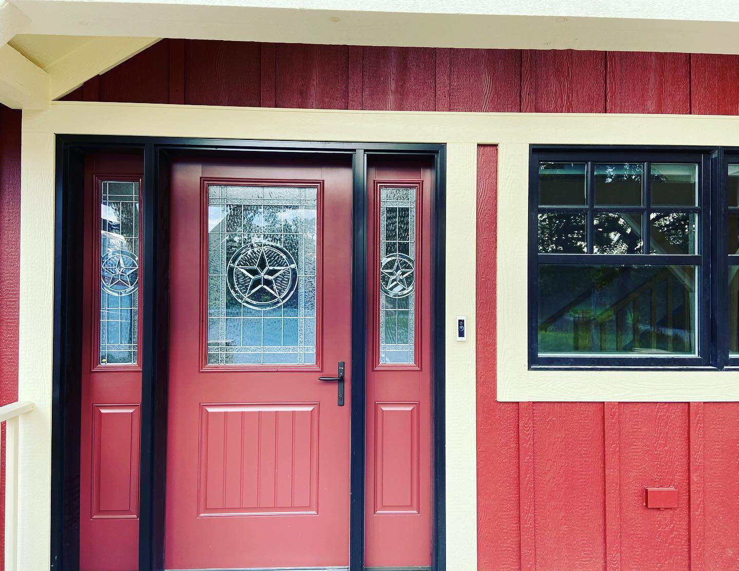 A red fiberglass entry door with decorative glass and black trim on a home with red board & batten siding.