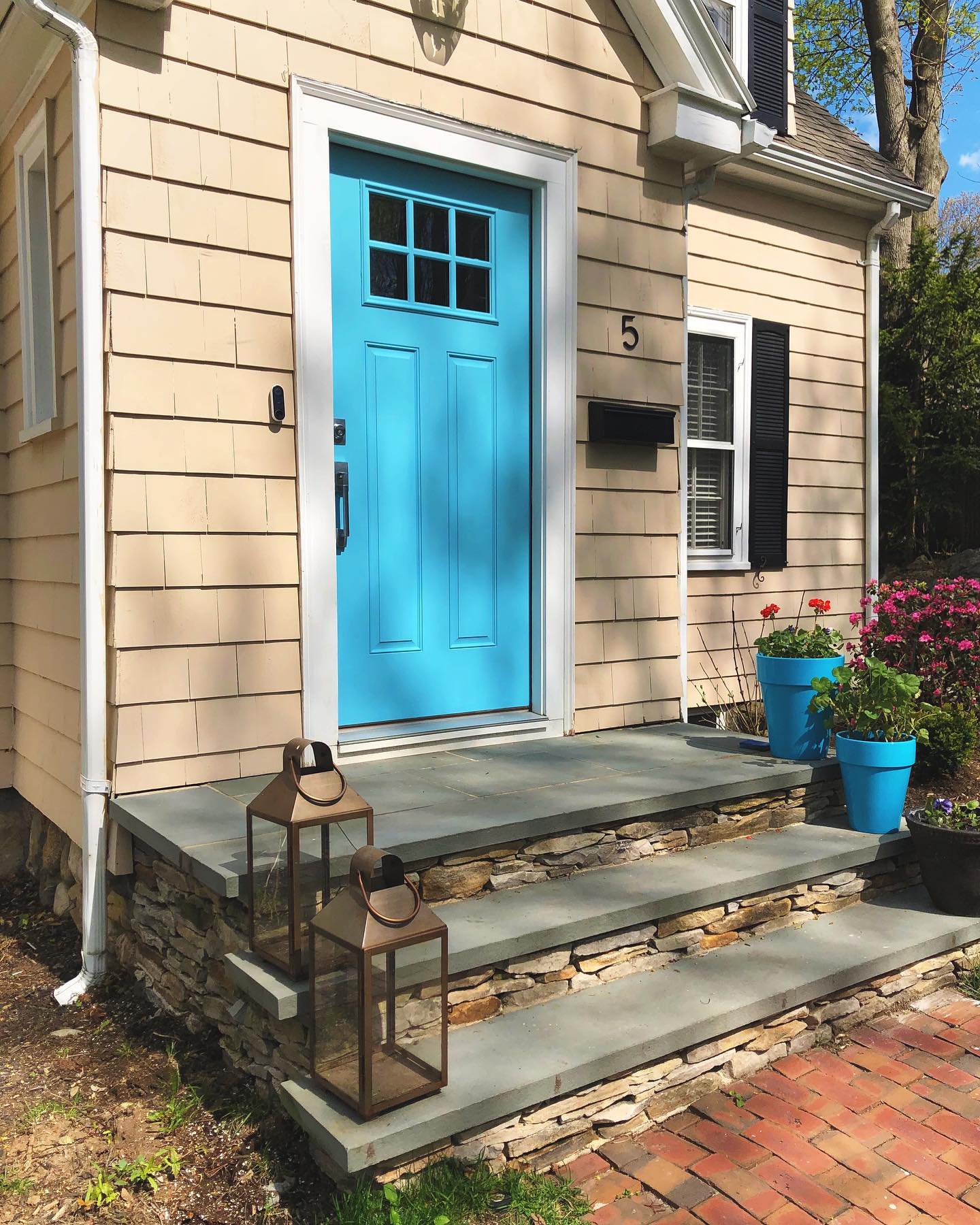 A bright turquoise fiberglass entry door on a home with light beige shake siding and stone stairs.