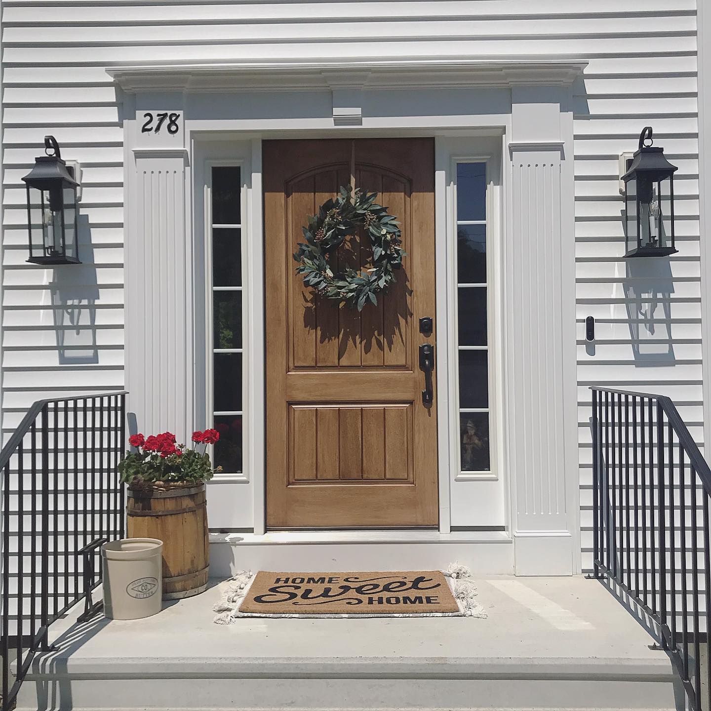 A wood entry door on a white home with a wreath hanging in the center of the door.
