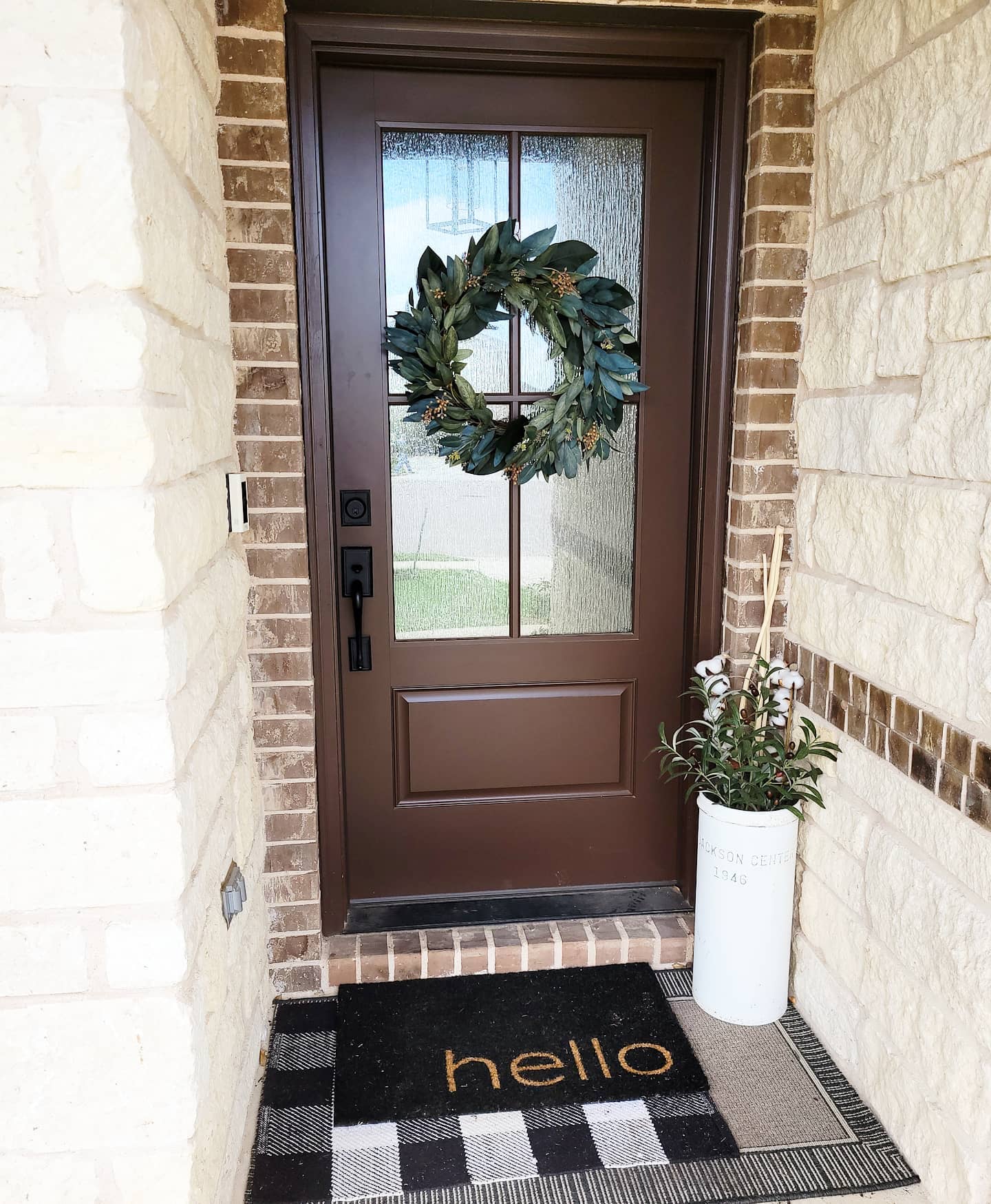 A wood entry door painted brown with 4 panes of frosted glass and a wreath hanging from the center of the panes.