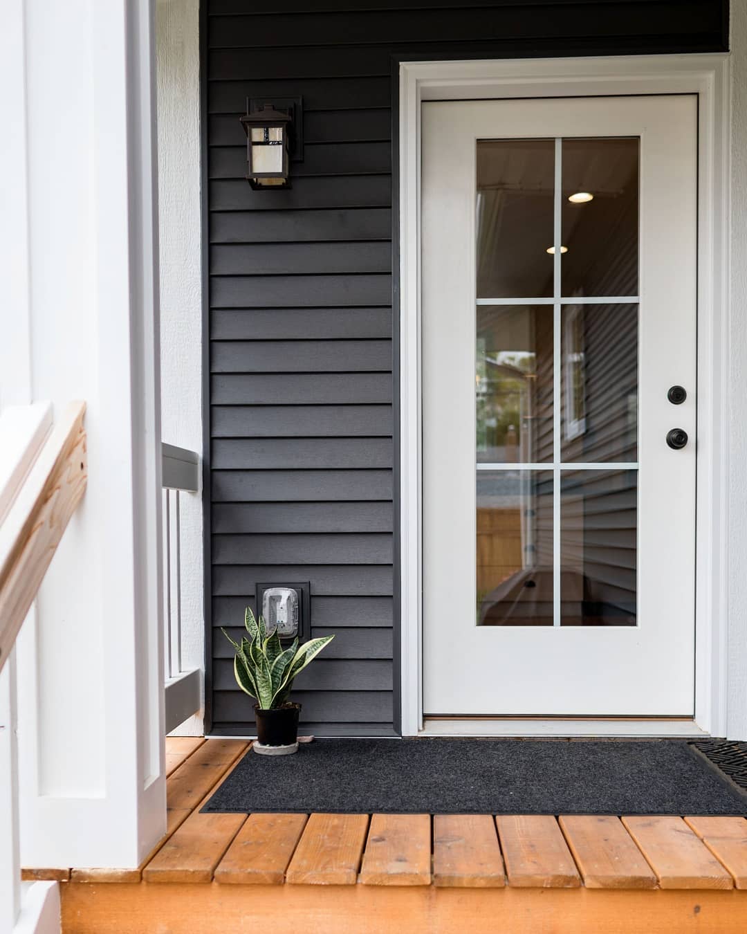 A white fiber glass entry door with glass panes on a dark gray home.