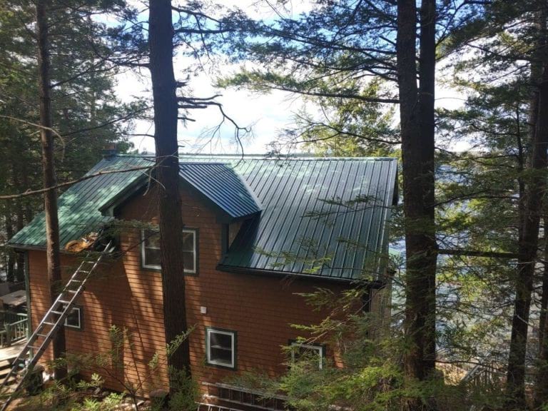 A ladder leaning against a home with a green metal roof and cedar shake siding.