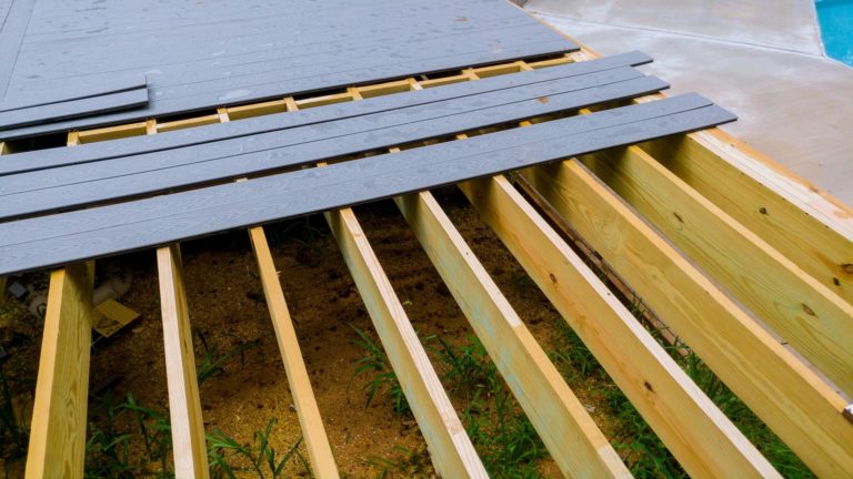 Gray composite decking panels being laid over a wooden framework.