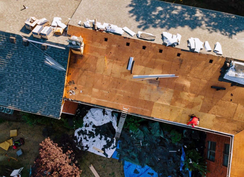 Workers repairing an asphalt shingled roof. Half the roof has been stripped down to the plywood.