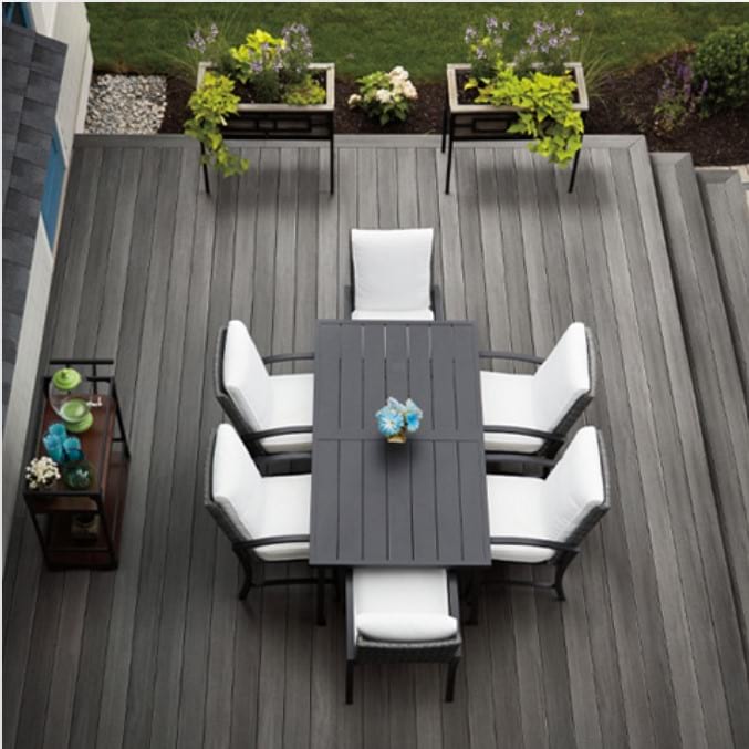 A gray composite deck with a gray table, 6 white chairs, and 2 plant boxes.