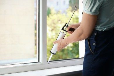 A person applying caulking to the interior of a window.