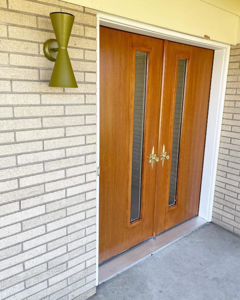 Double hinged wood doors with thin full length windows on a brick home with white trim.