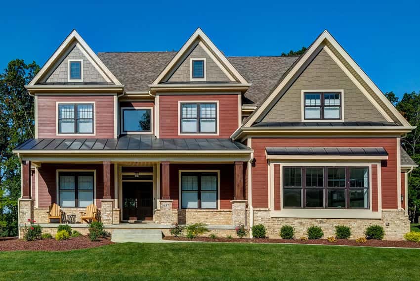 A large home with red clapboard and beige shake siding with stone accenting around the foundation.