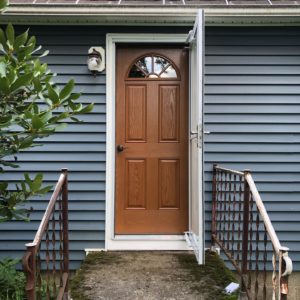 A white storm door opened exposing a wood entry door on a blue home.