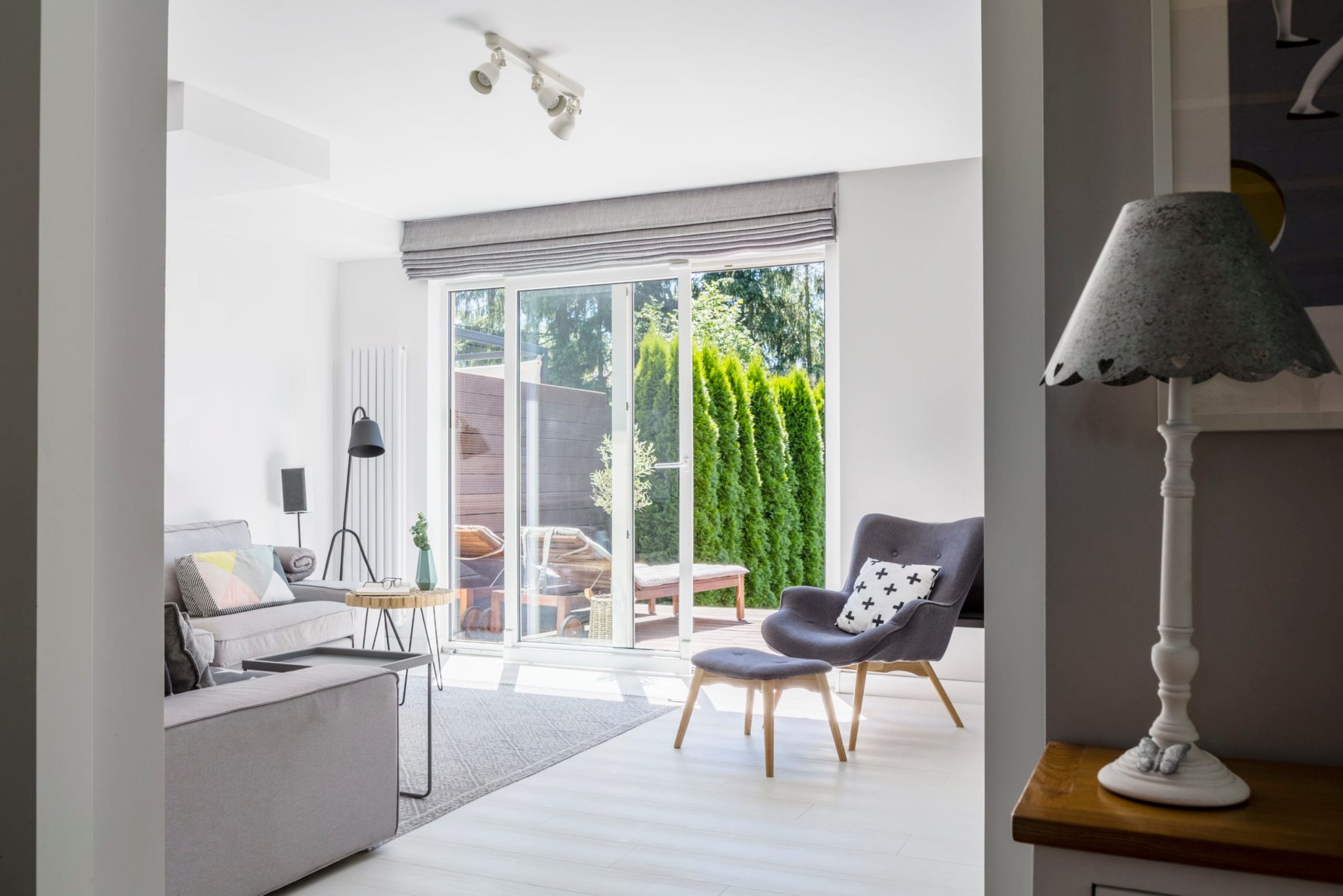 Lamp on cabinet and windows in white living room interior with glass sliding patio door in the background.