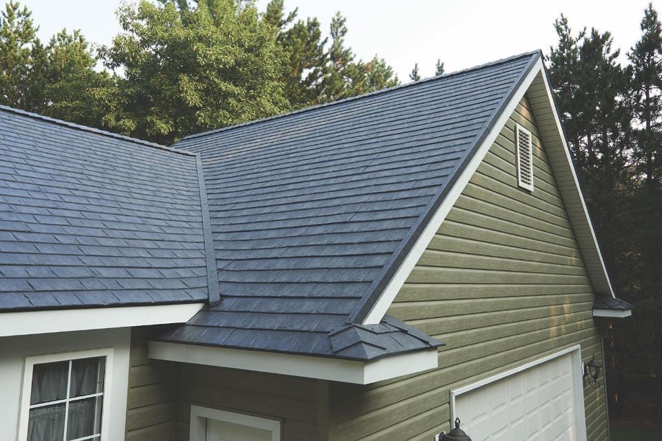 A green home with black metal shingle roofing and white trim.