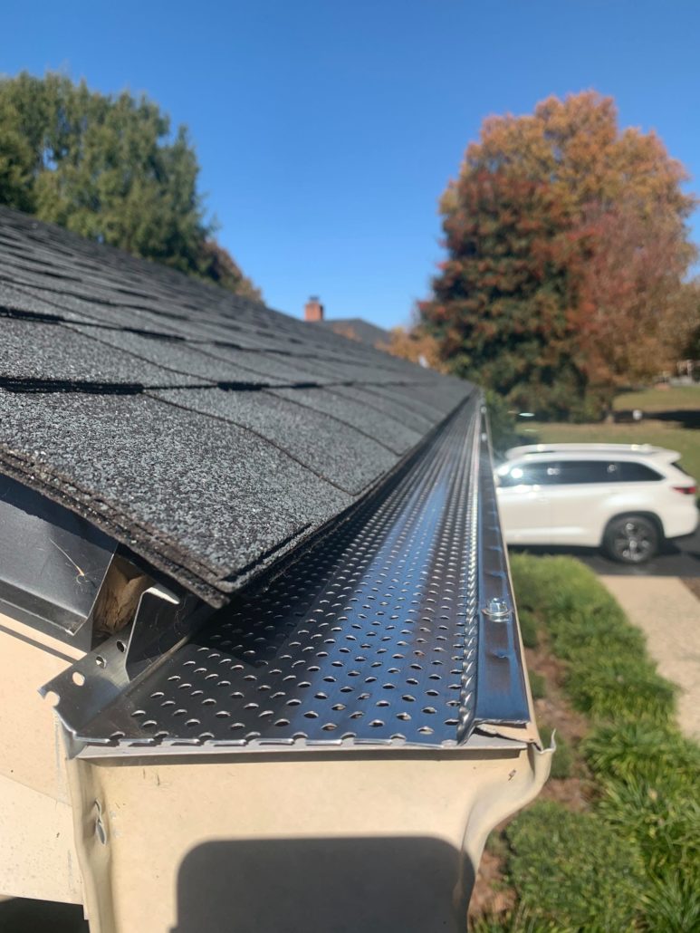 A black shingled roof with tan seamless gutters covered by gutter guards for protection against leaves.