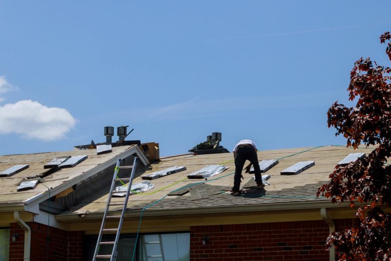 A roofer replacing shingles on a roof.