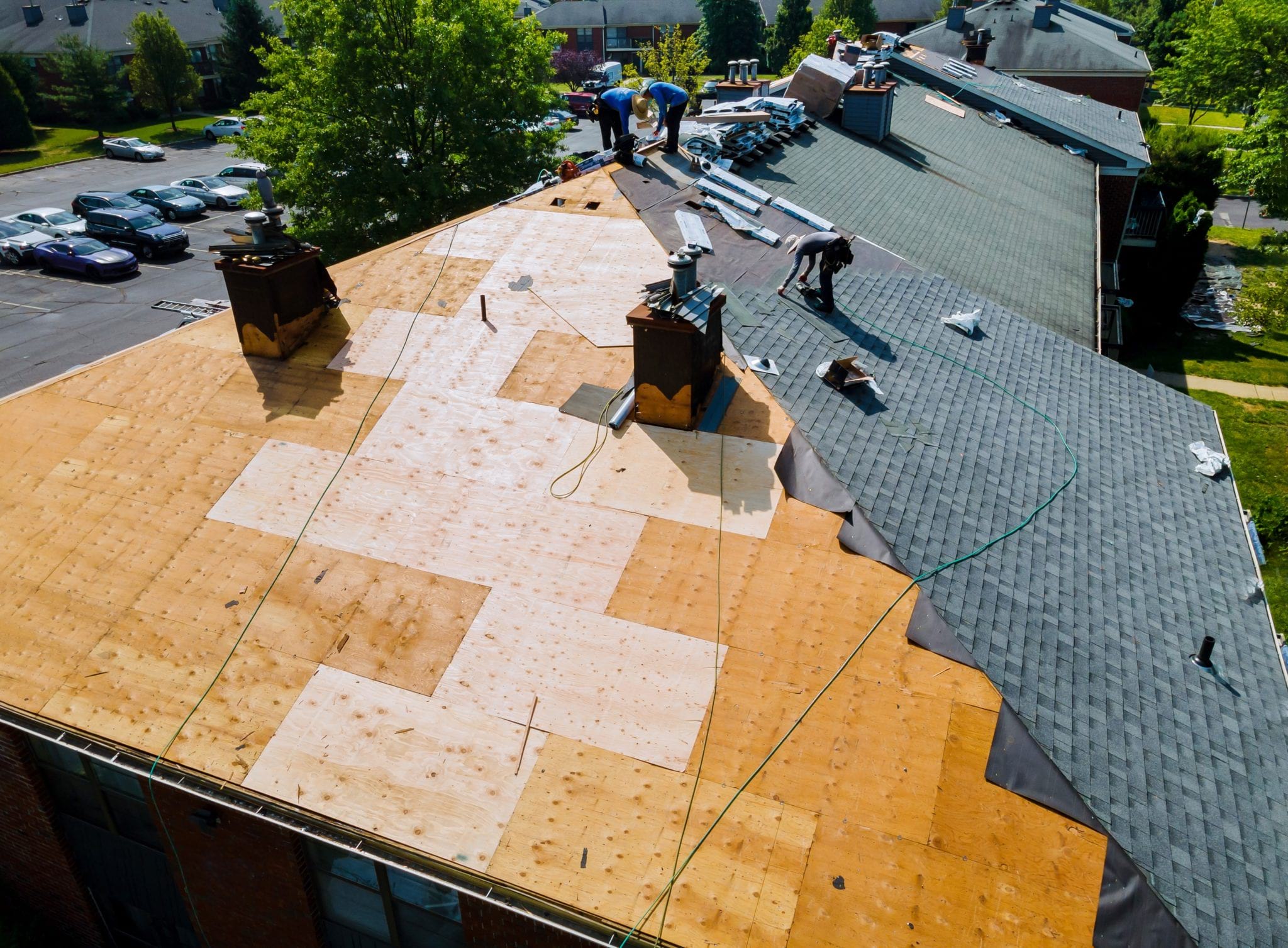 Workers repairing an asphalt shingled roof. Half the roof has been stripped down to the plywood.