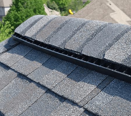 A roof's ridge vent covered by gray asphalt shingles.