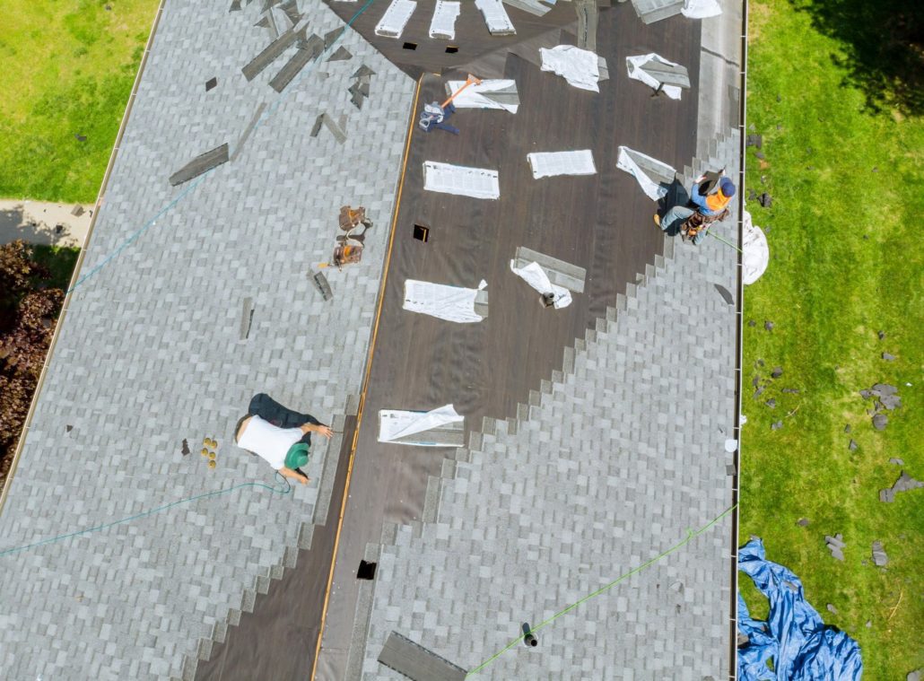 Roofers working on a roofing replacement on a gray shingled roof.