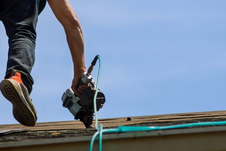 A roofer using a nail gun while working on a roofing repair.