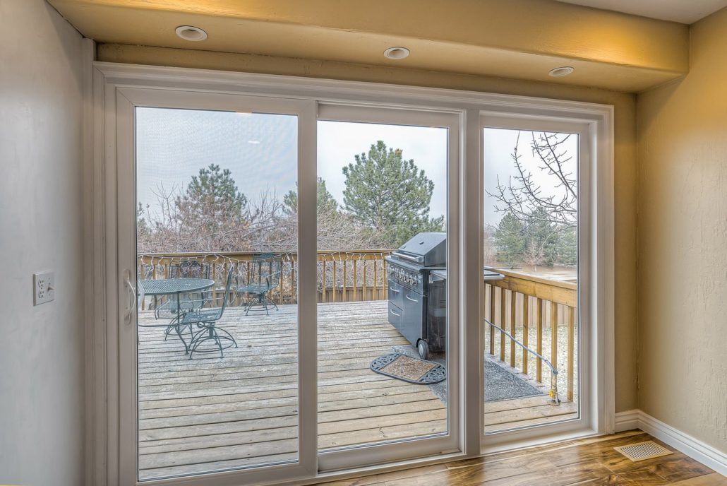 Sliding patio doors leading to a wooden deck with a grill and patio furniture.
