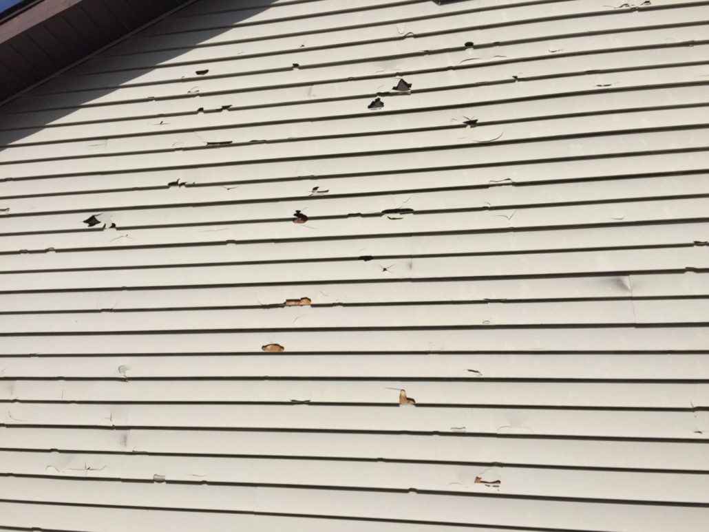 White vinyl siding with visible cracks and damage from a hailstorm.