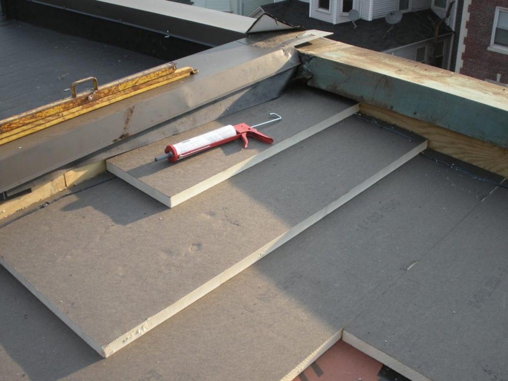 Tapered insulation on a flat roof with a caulking tool laid on top of the insulation.